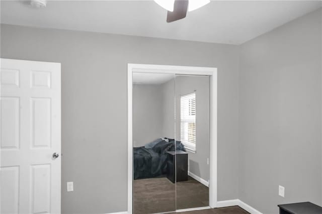 unfurnished bedroom with ceiling fan, a closet, and dark colored carpet