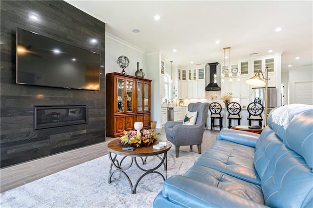 living room with light wood-type flooring, crown molding, and a large fireplace