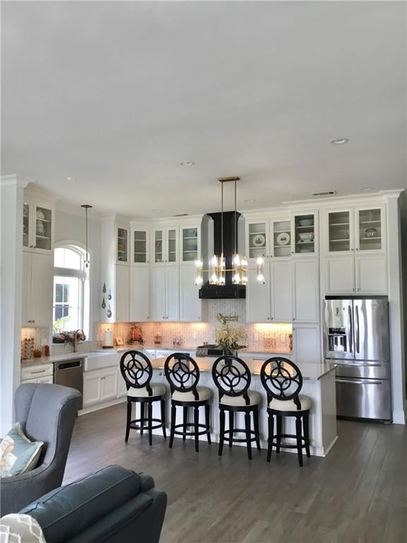 kitchen with appliances with stainless steel finishes, wall chimney exhaust hood, a kitchen island, dark hardwood / wood-style flooring, and pendant lighting