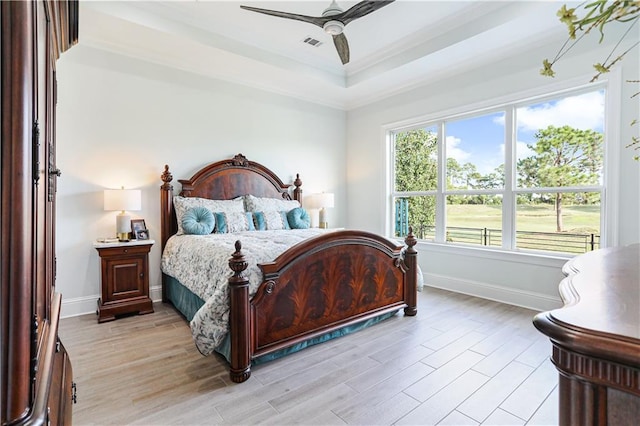 bedroom with ceiling fan, light hardwood / wood-style flooring, a raised ceiling, and ornamental molding