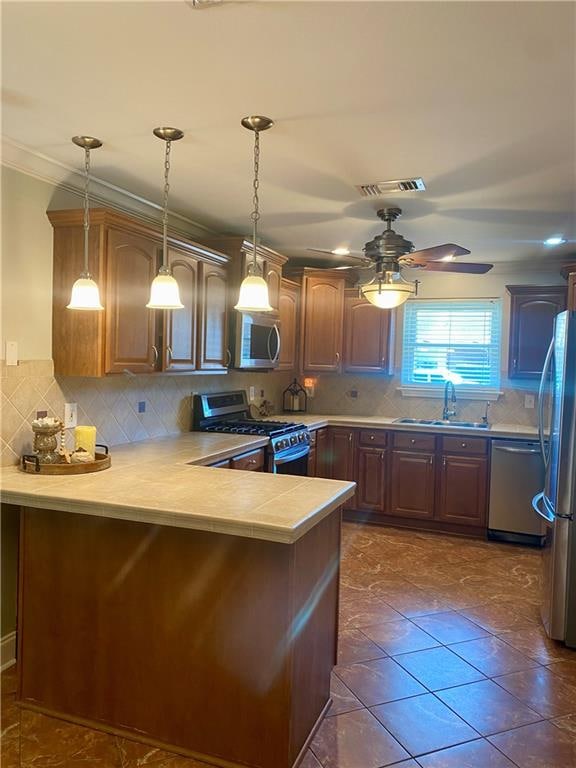 kitchen with appliances with stainless steel finishes, hanging light fixtures, kitchen peninsula, and tasteful backsplash