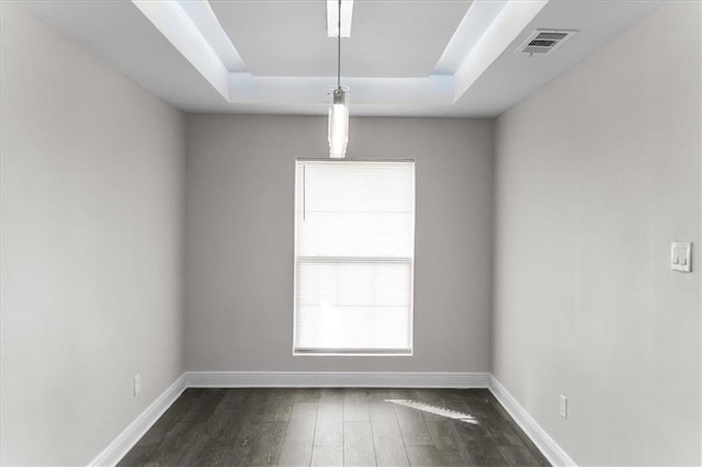 empty room with a tray ceiling, baseboards, dark wood-type flooring, and visible vents