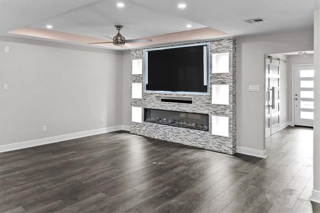 unfurnished living room with visible vents, a ceiling fan, a raised ceiling, baseboards, and a glass covered fireplace