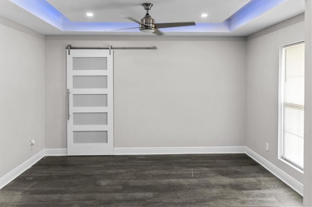 unfurnished bedroom featuring a tray ceiling, dark wood finished floors, a barn door, and baseboards