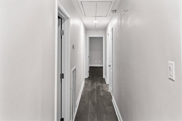 hall featuring baseboards, dark wood-style flooring, visible vents, and attic access