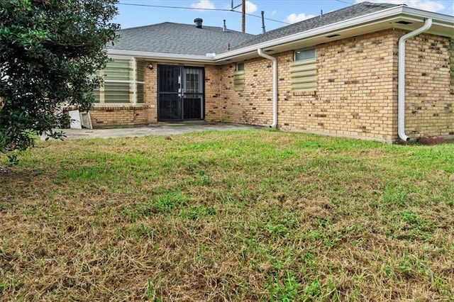 back of house with a yard, brick siding, and a patio