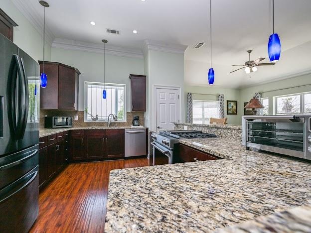 kitchen featuring light stone counters, decorative light fixtures, dark wood-type flooring, stainless steel appliances, and decorative backsplash