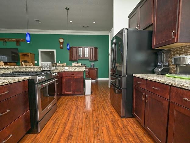 kitchen with dark hardwood / wood-style flooring, appliances with stainless steel finishes, decorative light fixtures, crown molding, and light stone countertops