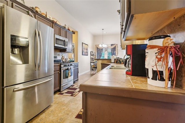 kitchen featuring tile counters, appliances with stainless steel finishes, decorative light fixtures, and sink