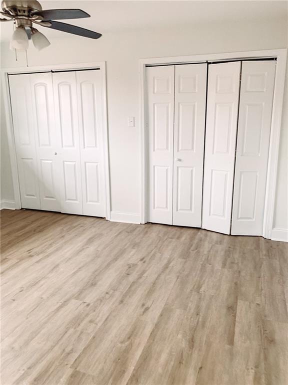 unfurnished bedroom featuring light hardwood / wood-style flooring, multiple closets, and ceiling fan