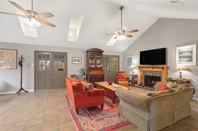 tiled living room with a tiled fireplace, ceiling fan, a skylight, and high vaulted ceiling