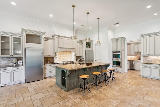 kitchen with appliances with stainless steel finishes, a kitchen breakfast bar, tasteful backsplash, decorative light fixtures, and a center island with sink