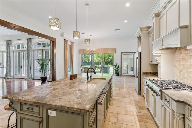 kitchen with a large island with sink, light stone countertops, stainless steel appliances, decorative light fixtures, and sink