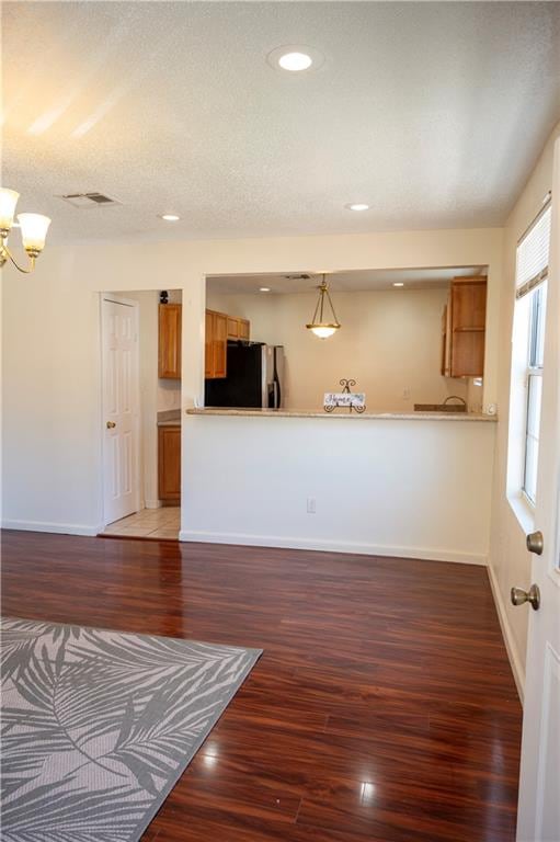 interior space featuring pendant lighting, kitchen peninsula, a textured ceiling, dark wood-type flooring, and stainless steel refrigerator