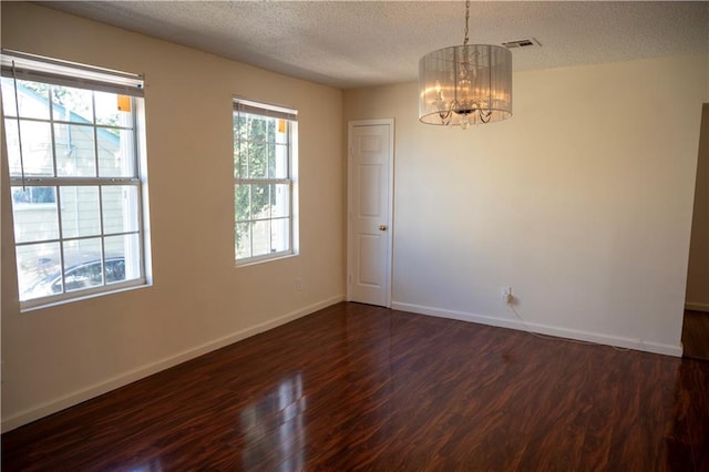 empty room featuring a chandelier, a textured ceiling, and dark hardwood / wood-style flooring