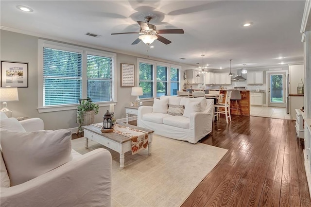 living room featuring ceiling fan with notable chandelier, light wood-type flooring, plenty of natural light, and ornamental molding