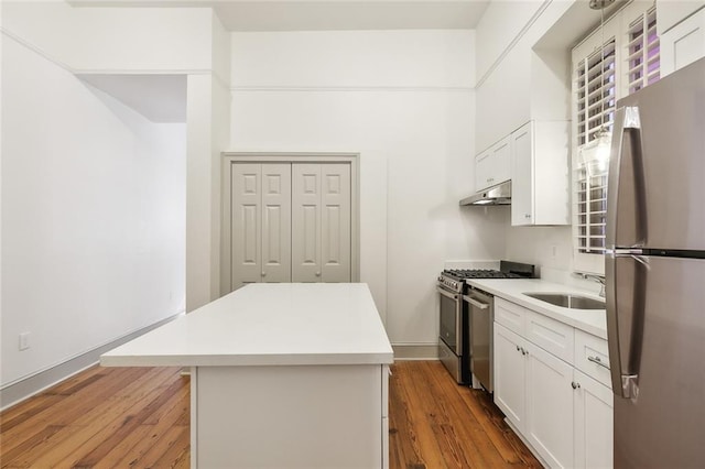 kitchen with white cabinets, stainless steel appliances, a center island, hardwood / wood-style flooring, and sink