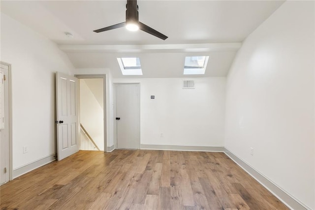 empty room featuring light hardwood / wood-style floors, lofted ceiling with skylight, and ceiling fan