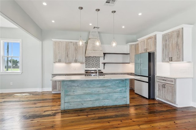 kitchen featuring dark wood-type flooring, hanging light fixtures, appliances with stainless steel finishes, and a center island with sink