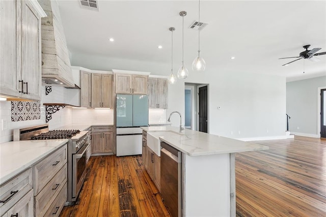 kitchen featuring a center island with sink, hanging light fixtures, dark hardwood / wood-style floors, appliances with stainless steel finishes, and premium range hood