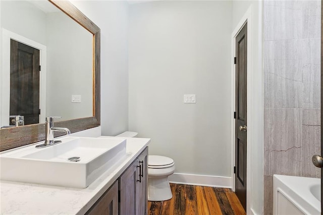 bathroom with a washtub, vanity, hardwood / wood-style flooring, and toilet