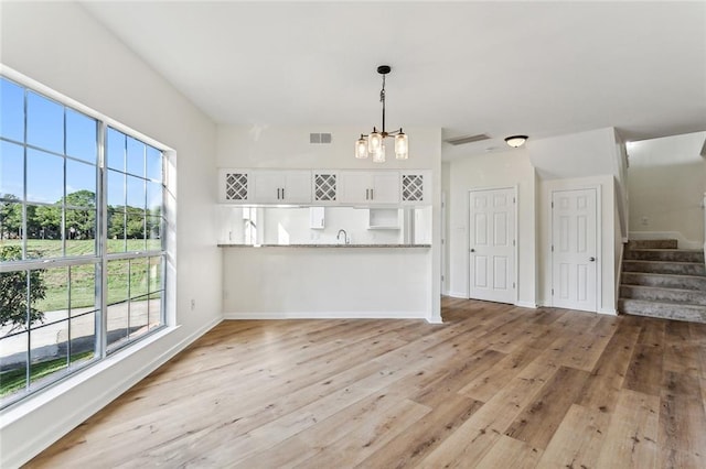 unfurnished living room with a wealth of natural light, light hardwood / wood-style flooring, sink, and a notable chandelier