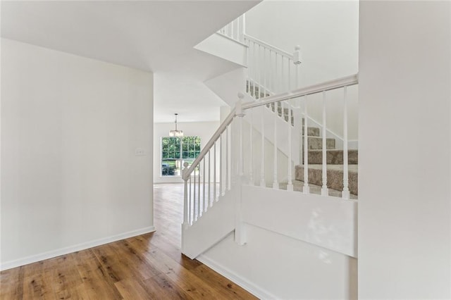 stairs with wood-type flooring and an inviting chandelier