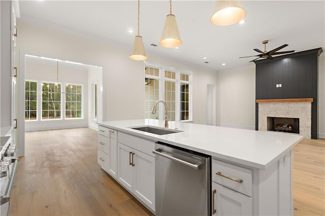 kitchen with stainless steel dishwasher, a center island with sink, white cabinetry, a fireplace, and sink