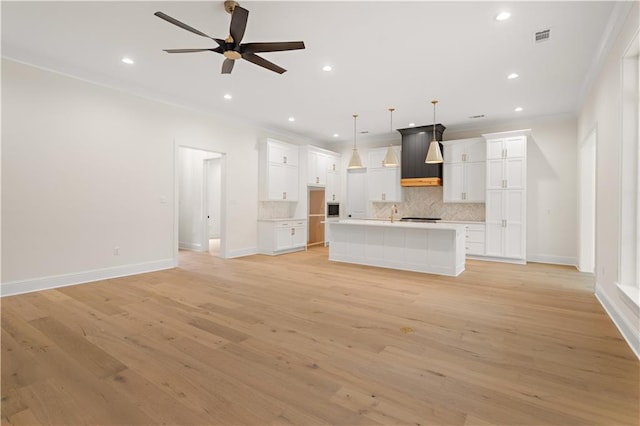 kitchen with white cabinets, ornamental molding, hanging light fixtures, and an island with sink