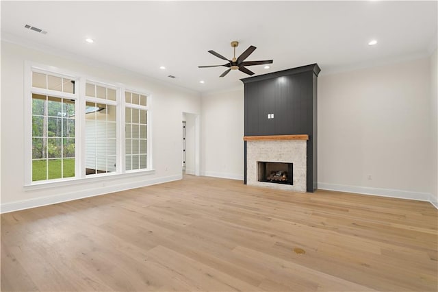 unfurnished living room with a large fireplace, ornamental molding, ceiling fan, and light hardwood / wood-style floors