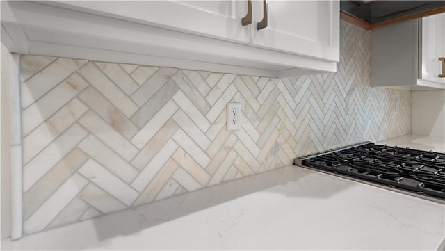 kitchen with white cabinets, decorative backsplash, stovetop, and light stone countertops