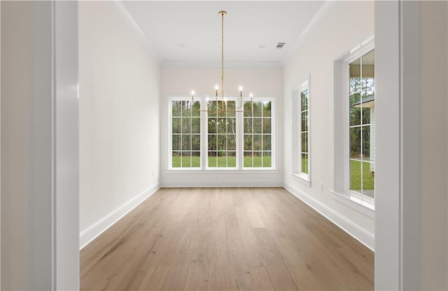 unfurnished dining area featuring a healthy amount of sunlight, light wood-type flooring, crown molding, and a chandelier