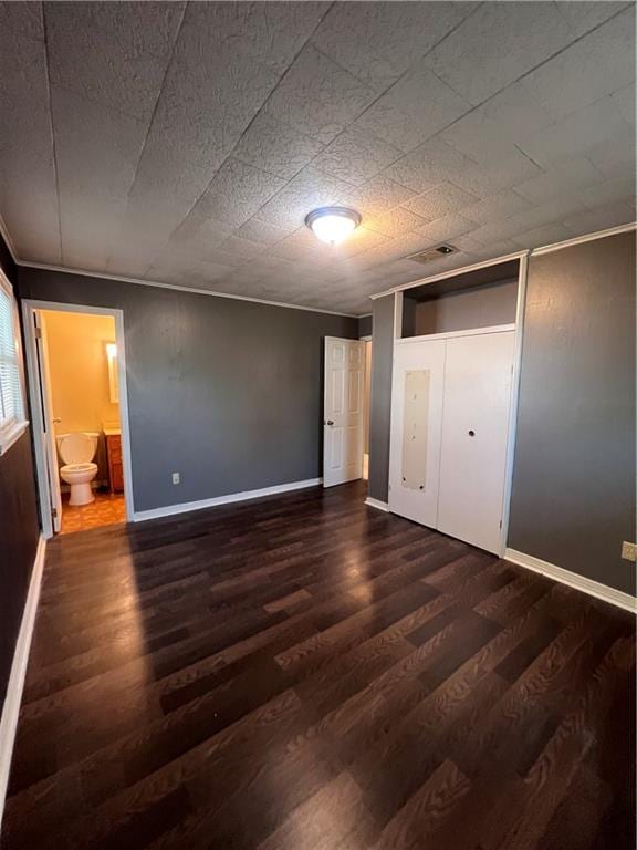 unfurnished bedroom with a closet, ensuite bathroom, and dark hardwood / wood-style flooring