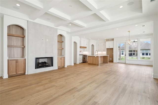 unfurnished living room with a multi sided fireplace, coffered ceiling, light hardwood / wood-style flooring, and beamed ceiling