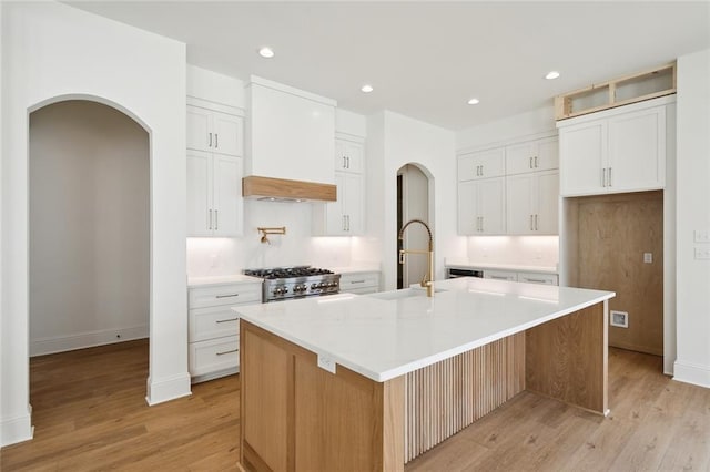 kitchen featuring light wood-type flooring, white cabinets, stainless steel stove, custom exhaust hood, and a spacious island