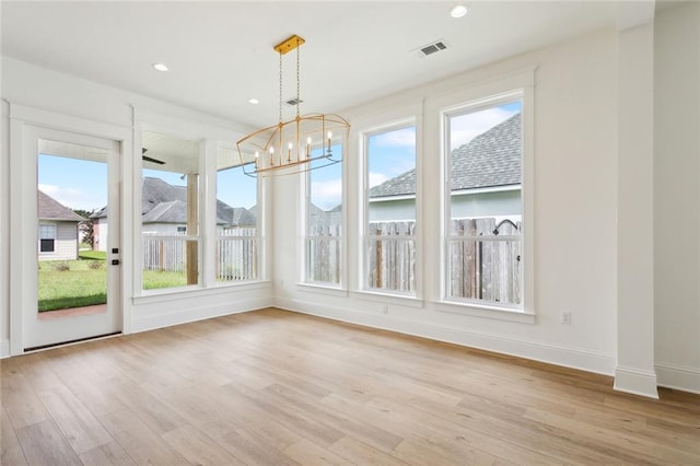 unfurnished dining area with a healthy amount of sunlight, an inviting chandelier, and light hardwood / wood-style flooring