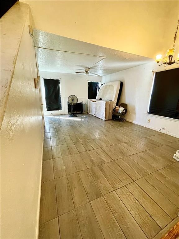 unfurnished living room featuring a textured ceiling, ceiling fan with notable chandelier, and wood-type flooring