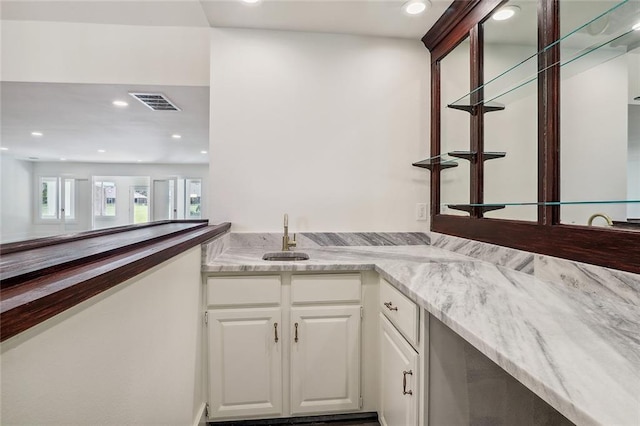 bar featuring sink, white cabinetry, and light stone counters