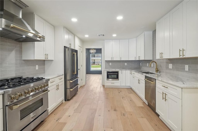 kitchen with white cabinets, sink, light hardwood / wood-style floors, wall chimney exhaust hood, and stainless steel appliances