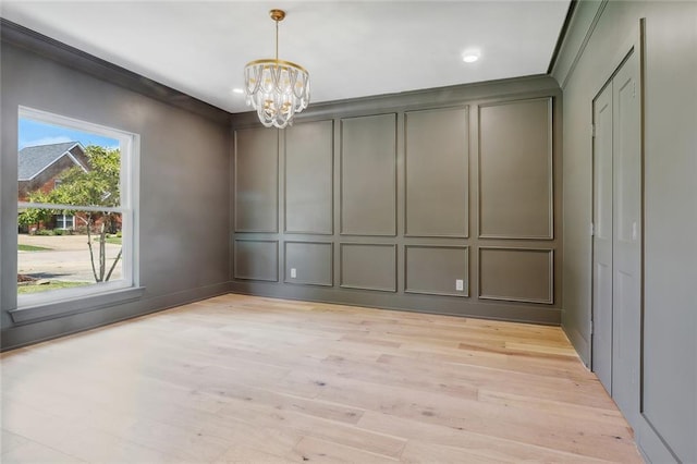 unfurnished dining area featuring a notable chandelier, light wood-type flooring, and crown molding