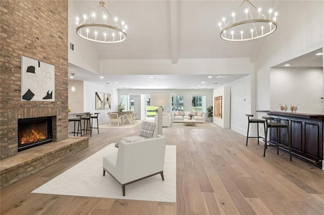 living room with beamed ceiling, light hardwood / wood-style flooring, an inviting chandelier, a fireplace, and a towering ceiling