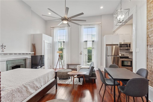 bedroom with ceiling fan with notable chandelier, dark wood-type flooring, and stainless steel fridge