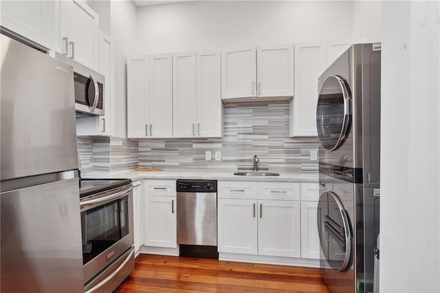 kitchen featuring appliances with stainless steel finishes, light stone counters, white cabinets, stacked washer and clothes dryer, and hardwood / wood-style flooring