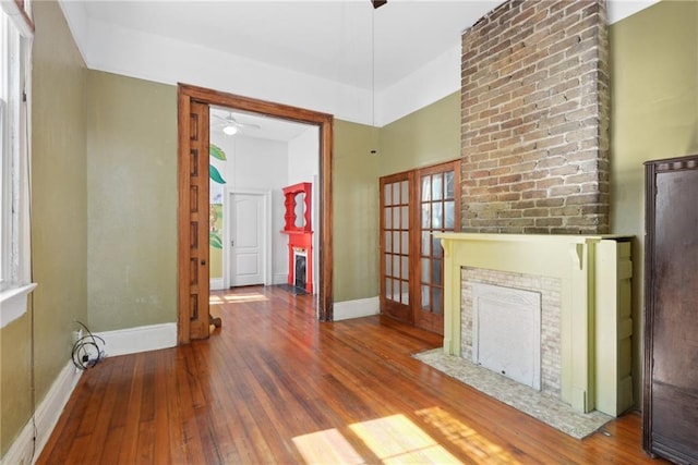 unfurnished living room with a brick fireplace, french doors, wood-type flooring, and ceiling fan