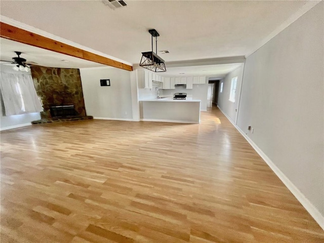 unfurnished living room with a fireplace, beamed ceiling, light hardwood / wood-style flooring, ceiling fan, and sink