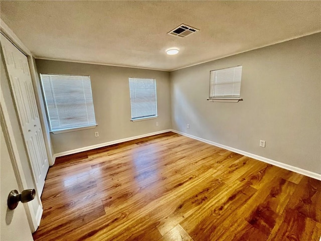 unfurnished bedroom featuring baseboards, a textured ceiling, visible vents, and wood finished floors
