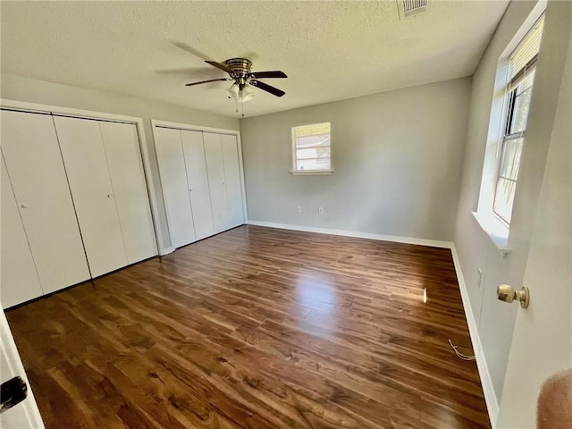 unfurnished bedroom with multiple closets, a textured ceiling, visible vents, baseboards, and wood finished floors