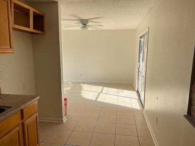 unfurnished dining area featuring ceiling fan, light tile patterned flooring, and a textured ceiling