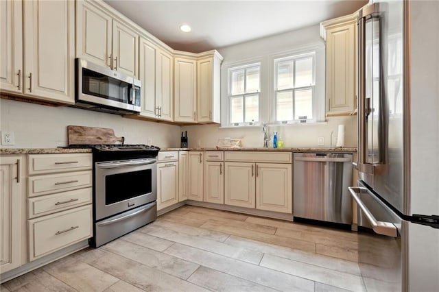 kitchen with cream cabinets, sink, stainless steel appliances, and light stone counters