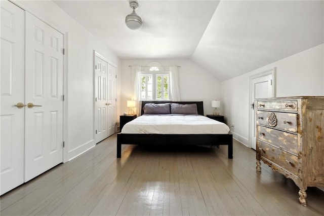 bedroom with light hardwood / wood-style floors, vaulted ceiling, two closets, and ceiling fan